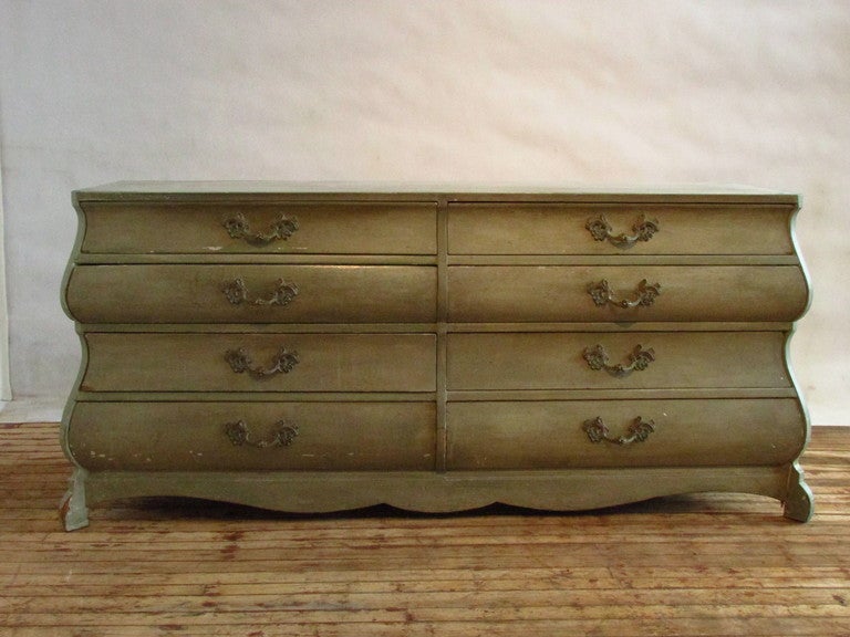 Exaggerated elongated bombay form with eight large drawers each with ornate brass hardware. the sides are decorated with raised shield panels. the chest is in old dry painted surface of pale mint blue green.