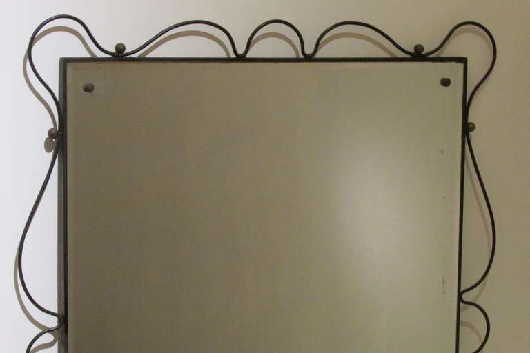 A large mid 20th century French modernist mirror in the manner of Jean Royere. The black painted wrought steel frame with brass ball decoration is in beautifully aged old surface. The original heavy plate glass mirror has areas of oxidation to
