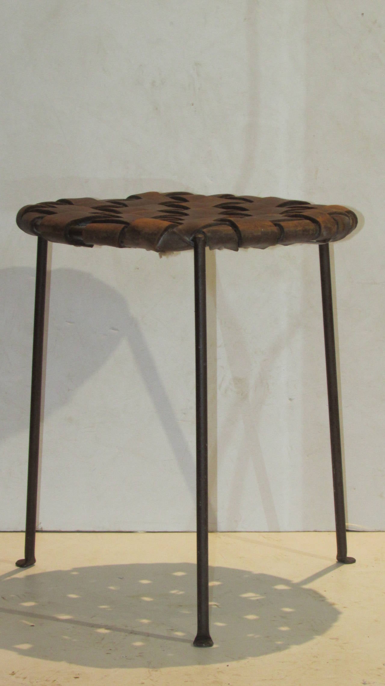 A beautiful original example of this hard to find three-legged pad foot hand-wrought iron stool with woven wide strap leather seat designed by Lila Swift and David Monell, American, circa 1950s.