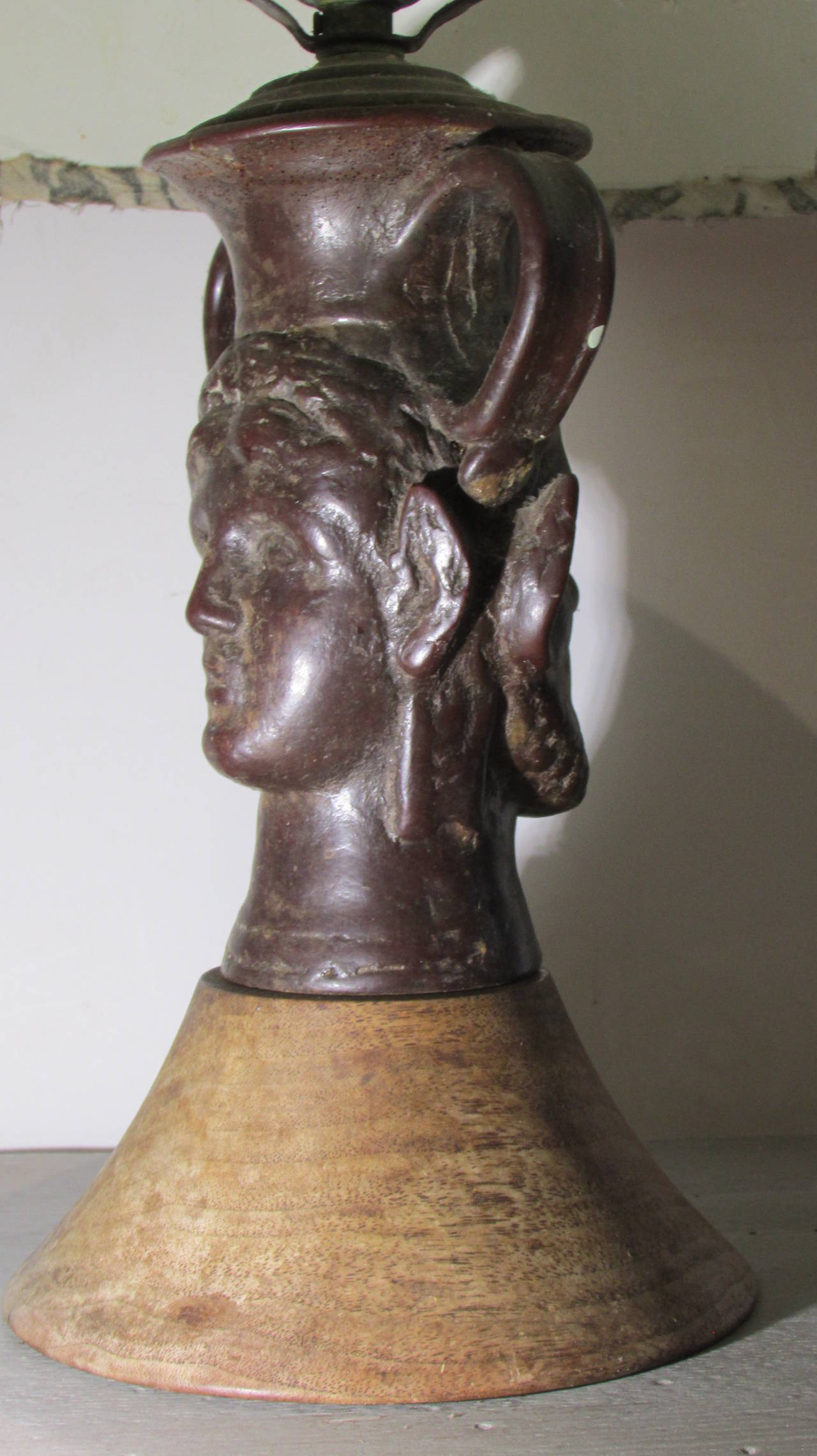 An unusual 1940s composition and wood table lamp in the surrealistic style of Jean Cocteau with a classical face on one side and a devilish satyr face on the other side. The shade covered in vintage Fortuny fabric.