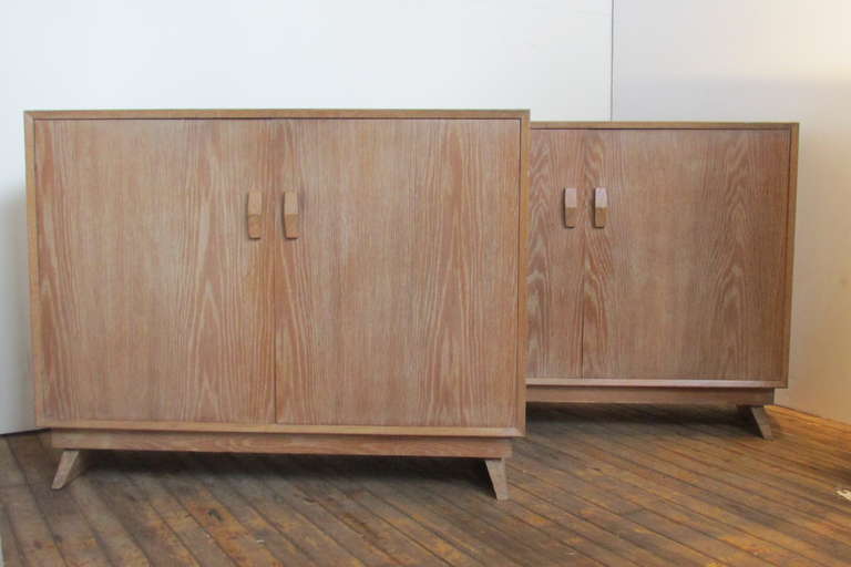 A straightforwardly elegant pair of French 1940's style modernist cabinets in the original cerused finish with all over beautifully aged pale color to wood grain. The chests with two doors / adjustable interior shelves / raised on angled plank feet.