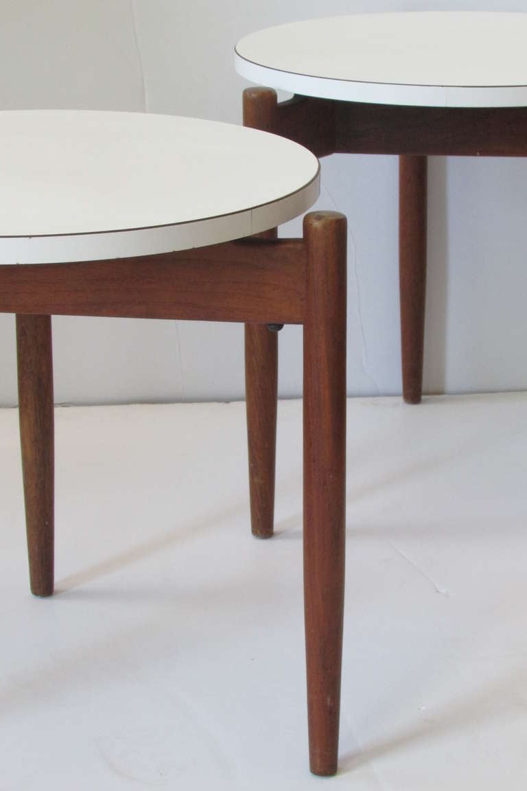 A pair of mid century Jens Risom Design stacking tables with the original period labels. The round white laminate tops raised on three tapered walnut legs.