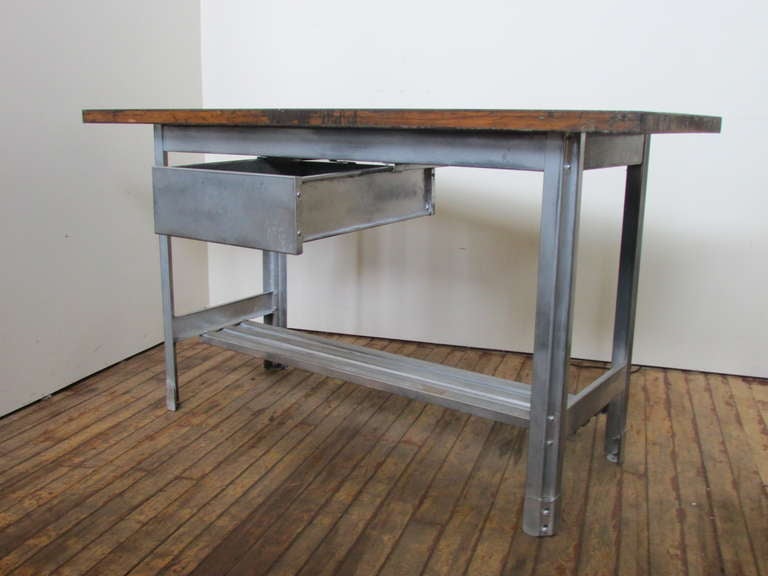 Old industrial factory work table. Milled polished aluminum metal base w/ a large deep central sliding drawer and a lower narrow stretcher shelf. Original wood top with deep rich color and beautifully aged patina and wear from years of use. Not to