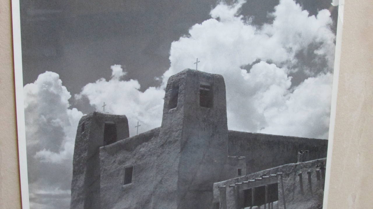 In the style of Ansel Adams  - a vintage black & white photograph of an old New Mexico mission church in stark landscape with large cumulus clouds in sky.