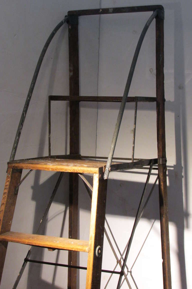 An antique American industrial safety folding ladder with top platform. Beautifully aged wood & steel construction with a finely detailed architectural scaffold like form.  A perfect utilitarian work / library ladder as well as a decorative display