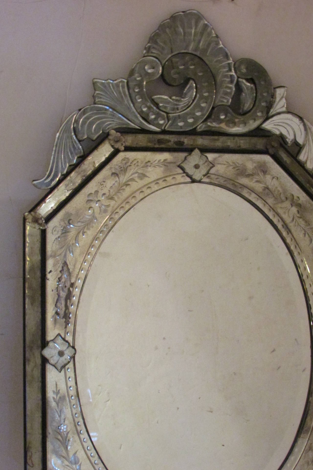 A large octagonal form Venetian mirror with a finely etched mirrored framework and asymmetrical top and bottom acanthus form crests. The interior oval mirror glass with bevelled edges. The entire mirror with beautifully aged desirable oxidation to