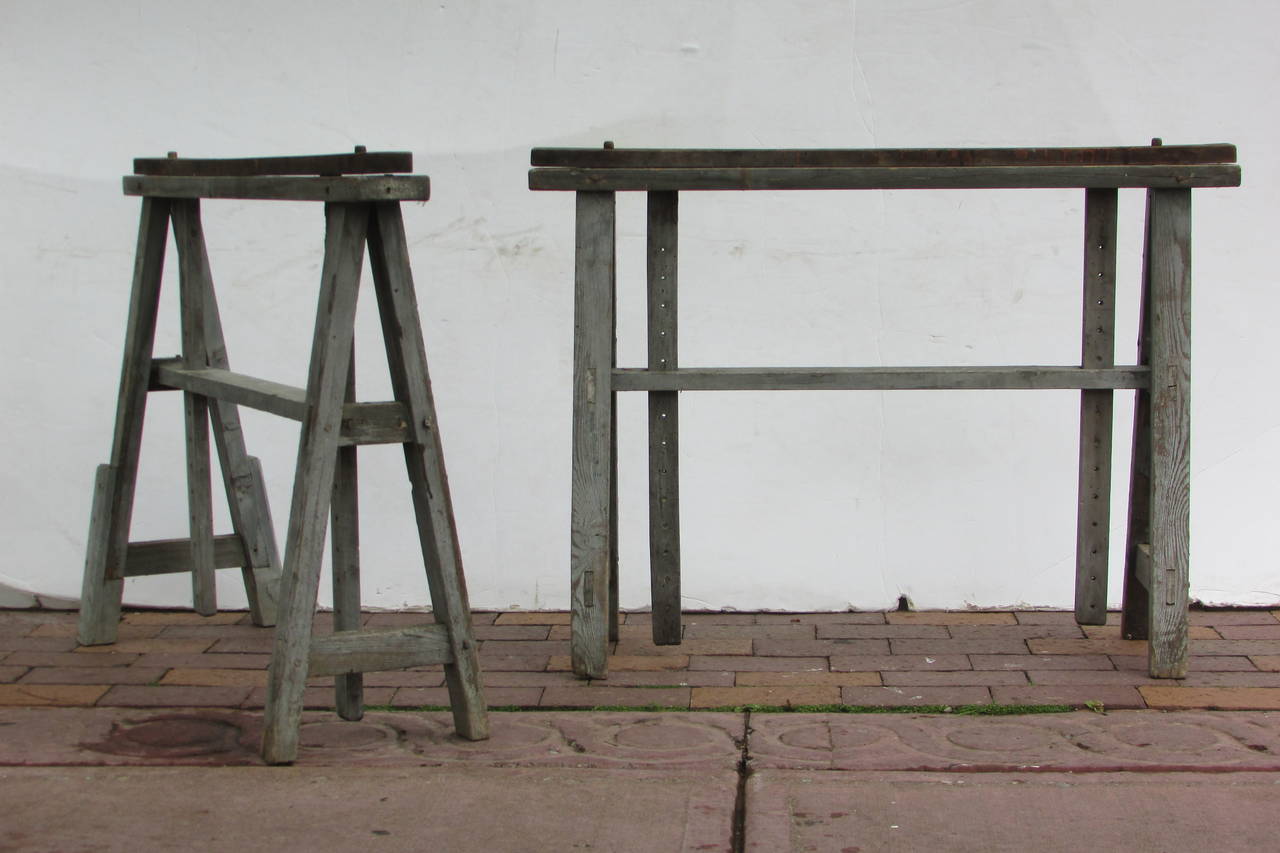 A pair of rare antique metamorphic wood sawhorses in original beautifully aged worn driftwood gray painted surface with wood pegged and mortised  construction. The adjustable top rails can be easily positioned to many different heights and angles by