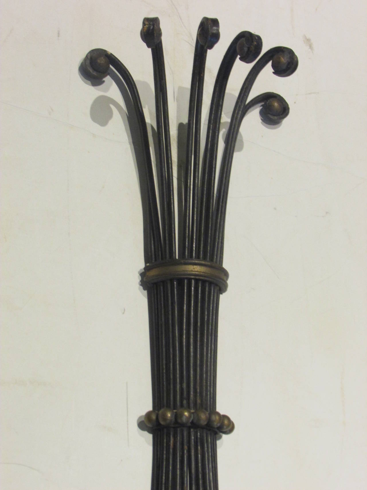 In the style of Jean Royere, A large sculptural black painted iron wall shelf decorated with inset gold metal balls at curled iron top above a curved brass ring banding / a curved ring of gold metal balls and a large brass urn finial at bottom,