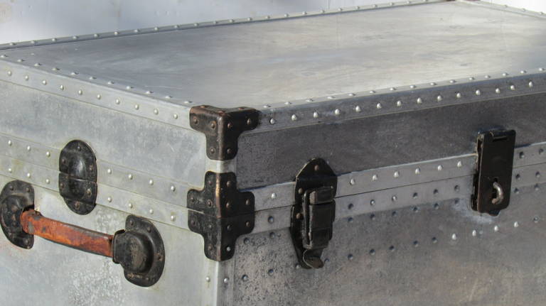 A heavy gauge industrial aluminum riveted trunk with black metal locks and fittings, painted metal lining, large fitted compartment tray, leather handles. Good original old surface color and age expected wear yet with barely a ding or a dent. Locks