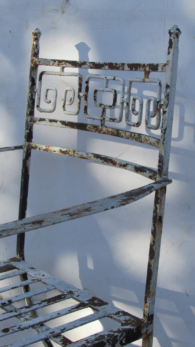 An exceptionally beautiful set of four neoclassical Curule form hand-wrought iron garden chairs with Greek key design backs / curved arms and slatted seats. They are in old worn and distressed white painted surface from years of outdoor use. All