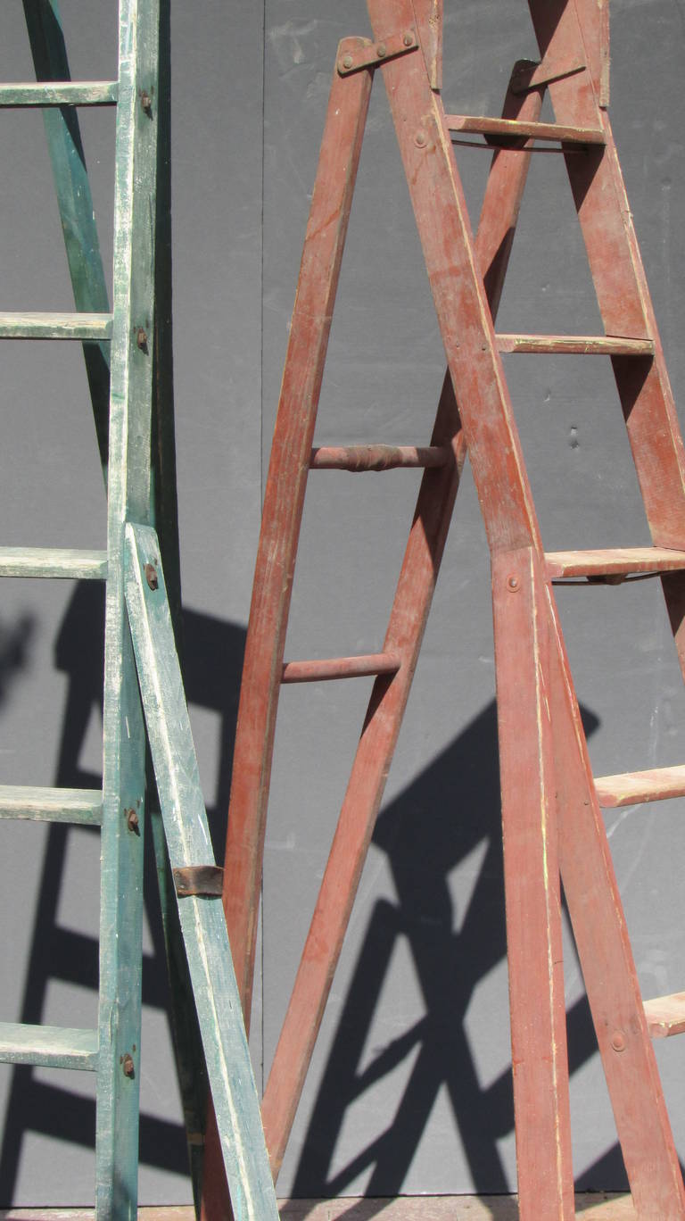  Antique three legged wood folding orchard ladders. Both with beautifully aged original dry painted surface color and an architectural sculptural easel like form. Structurally solid strong for utilitarian use - harvest, garden, library or as