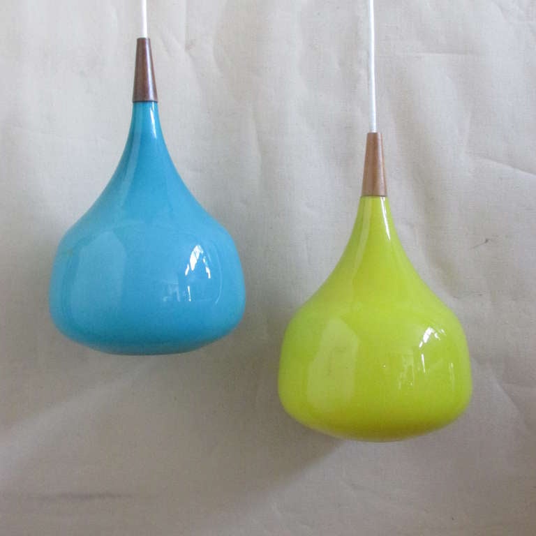 Teardrop form azure blue and canary yellow glass and teak pendant lights. Glass pendants are 8.5 inches wide x 11 inches high & 14 inches high with the teak caps. Working order with plugs for electric. * BLUE PENDANT IS SOLD *