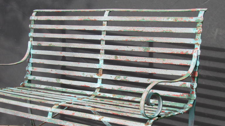 Antique strap iron classical form garden bench with hand-wrought and riveted construction showing a nicely aged layering of various colors painted over the years. Structurally solid and strong.
