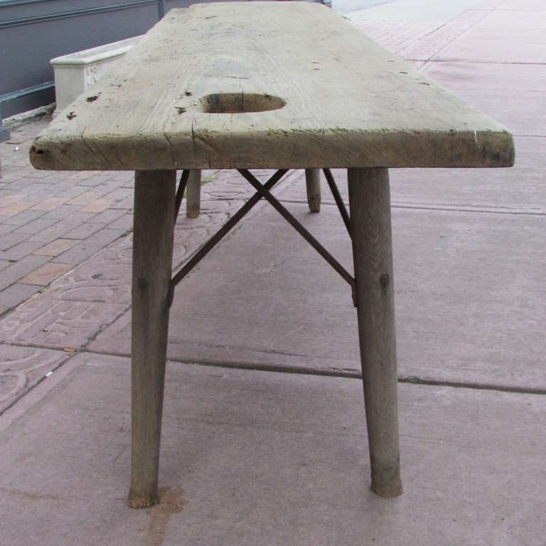 American farmworker's harvest table with a 1.5 inch thick single board top. There is an oval hole at one end of the top for disposal of excess cuttings as well as some small holes for utensils. Opposite end with one angled side / a rectangular cut