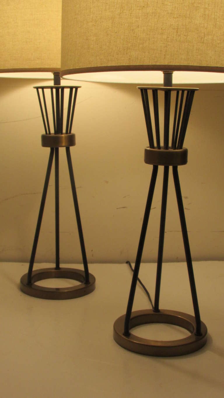 A pair of mid 20th century modern tripod table lamps with nicely aged original surface to the black enamel painted metal rods and brass rings. These lamps are often attributed to Gerald Thurston for Lightolier or Laurel. The shades for display