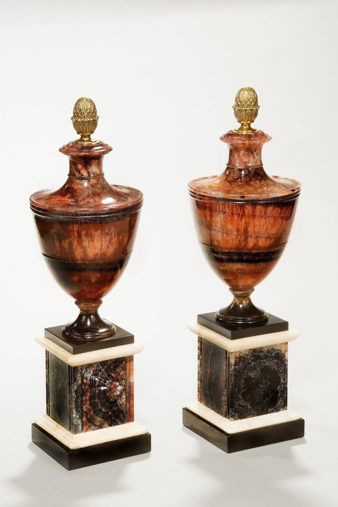 A large pair of Blue John chimney ornaments, English circa 1790-1800. Derbyshire spa statuary marble and Belgian black marble. Each neoclassical urn shape ornament has a pineapple gilt brass metal finial which is a possibly later. The urn is raised