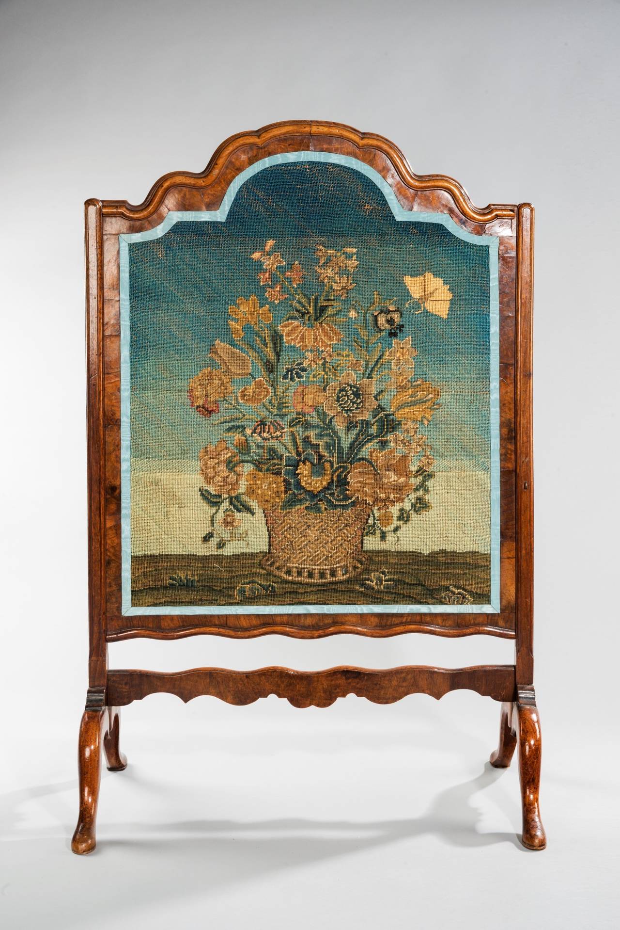 A beautiful needlework panel of flowers in a large urn or basket woven container and a large oversized butterfly in flight. The whole is housed in an 18th early 19th century walnut end support fire screen frame, which slides up and down and has