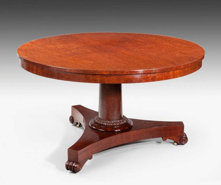 A circular tilt-top mahogany plum pudding veneered breakfast table, supported on a very plain and elegant column with carving around the lower section. The whole is raised on a concave-sided triangular base with concealed castors. English circa 1835.