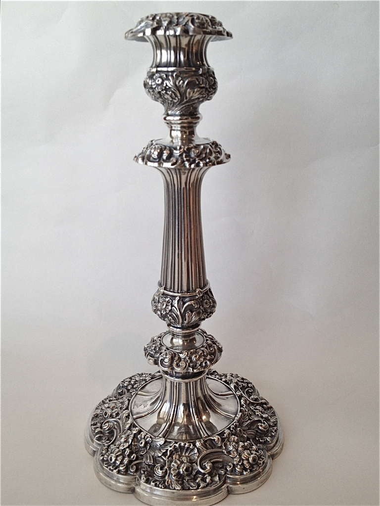 A fine pair of candlesticks decorated with repousse flowers and leaves with a fluted standard then elaborate decoration corresponding to the work below with a coat of arms on the base and on the bobeches all hallmarked and in beautiful condition