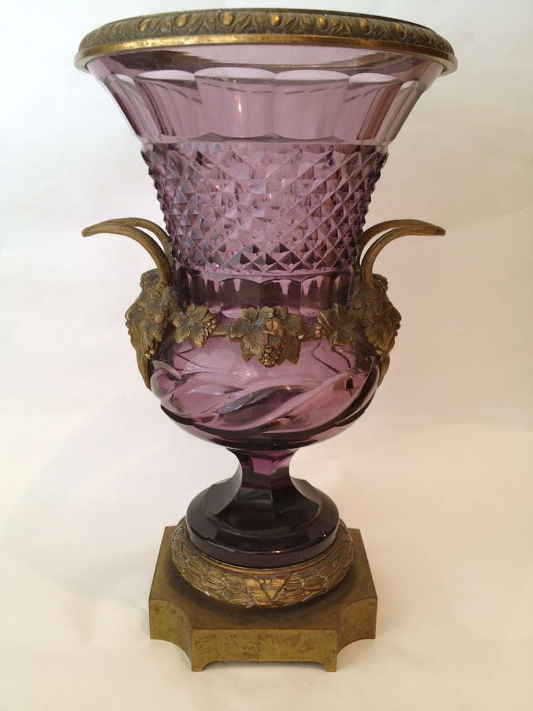 Gilt bronze masks of Bacchus flank the sides of these rare amethyst color cut glass urns, the cut is complexed and the campaign shape is classic.