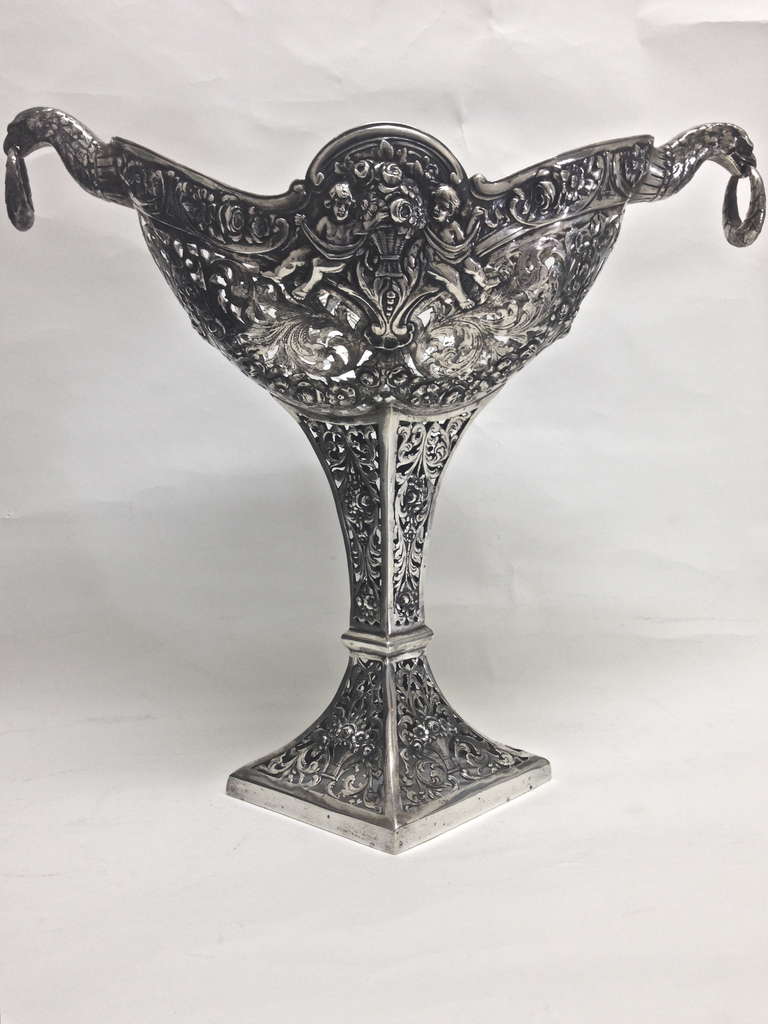 A lovely German 800. silver centerpiece decorated in repousse with putti and flowers, finely cast and chased flanked with bird heads holding rings in their beaks.