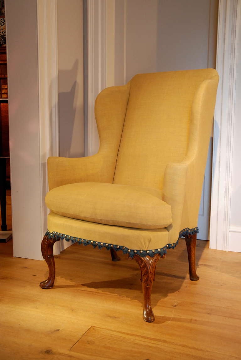 A finely shaped George I walnut wing chair, the front cabriole legs finely carved  of good colour and patination, upholstered in mustard colour linen with a fine petit point needlework cushion. Circa 1725