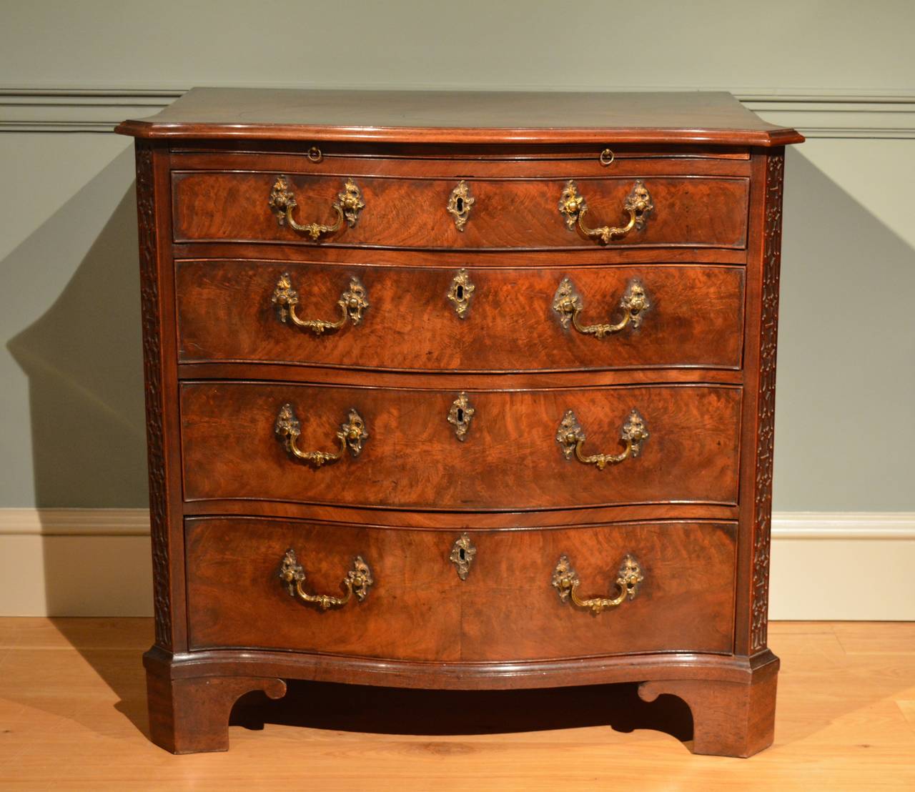 A fine small George III mahogany serpentine chest of four drawers, having blind fret to the canted corners, the drawers with Rococo handles and escutcheons, standing on bracket feet. This piece has finely figured veneers of excellent colour and