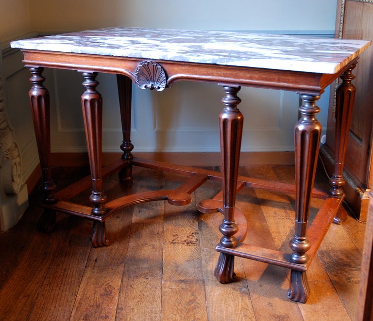 An early 18th century side table, the breche violette marble top above a mahogany base of rare Baroque form, the shallow frieze centred by a carved shell, the tapering flutted legs united by straight and curving stretchers, the whole standing on