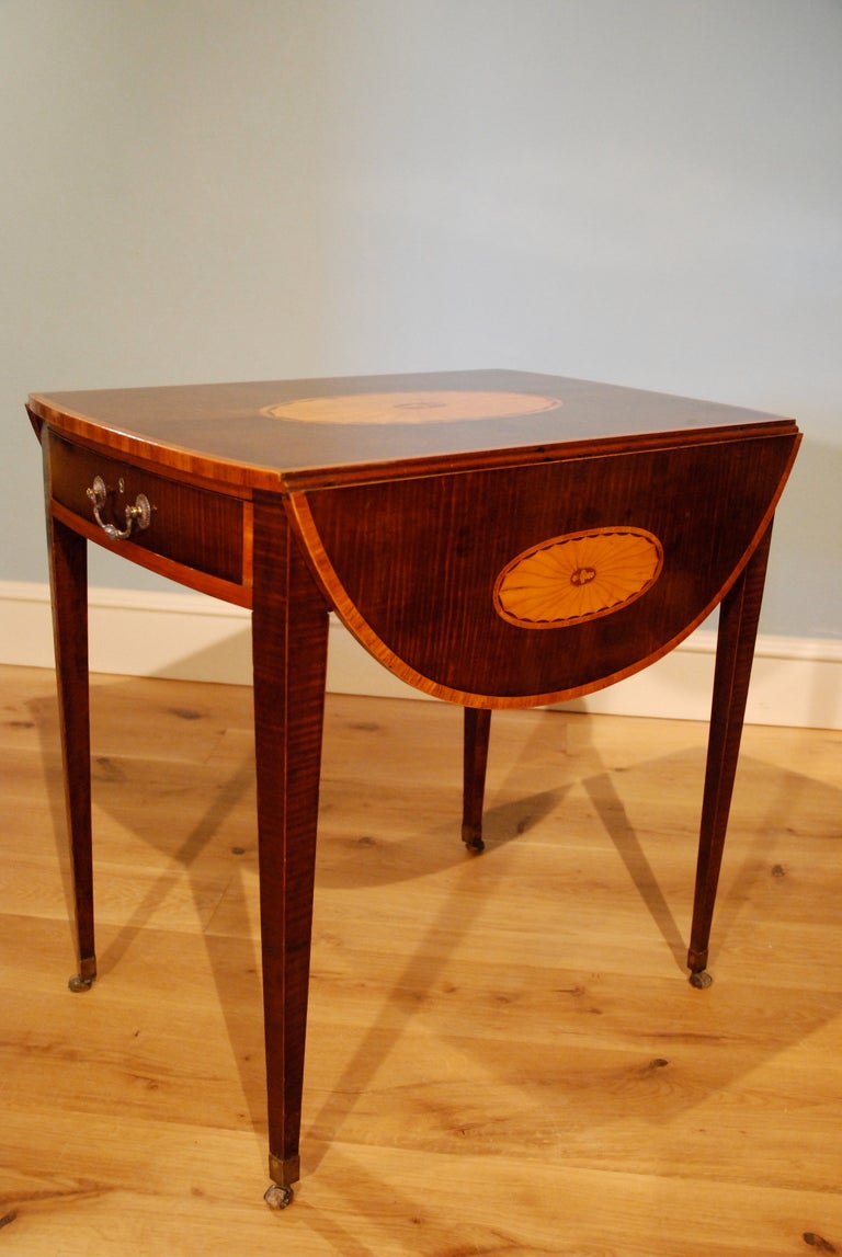 A late 18th Century Pembroke table veneered in harewood, the top crossbanded and inlaid with Neo-classical fan motifs. The drawer containing a baize lined writing slide. Circa 1790.