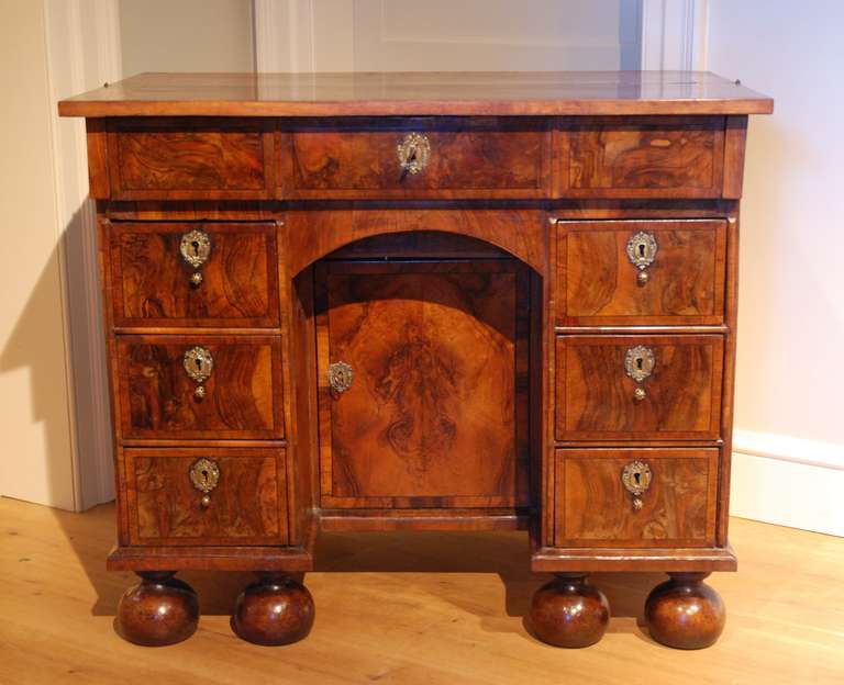 A rare William and Mary olive wood and walnut veneered kneehole desk, the front half of the top hinging back to reveal, with a fall front, a fitted writing area enclosing six small drawers, below which is an arrangement of six drawers surrounding