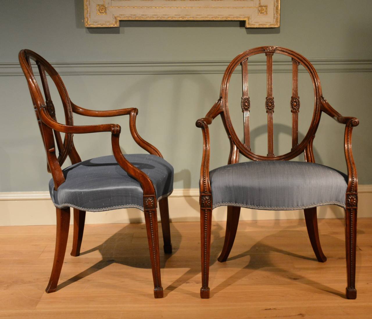 A pair of 18th Century mahogany armchairs, the oval backs out swept arms and tapering front legs, all finely carved, and retaining their original patination, with stuff over seats, in blue silk. English  Circa 1780