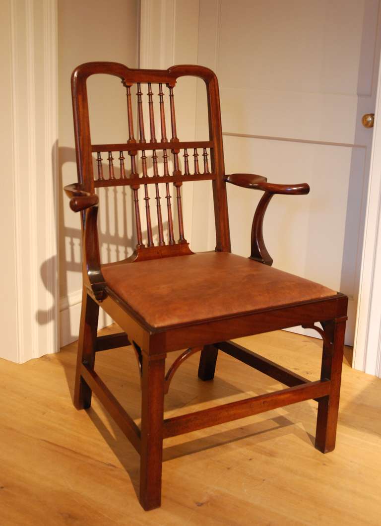 A George III mahogany desk armchair of unusual form, the back containing spindles set in a cruciform pattern, the well shaped and detailed short arms allowing easy access in and out from a writing position standing on straight legs with original