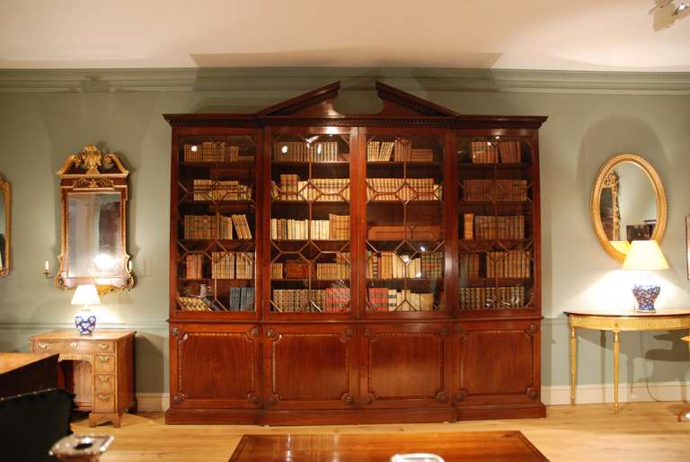 A very fine 18th Century architectural mahogany breakfront bookcase having a broken arched pediment and dental frieze above four glazed doors containing their original glass, the lower section having crossbanded fielded panels, carved rosettes to