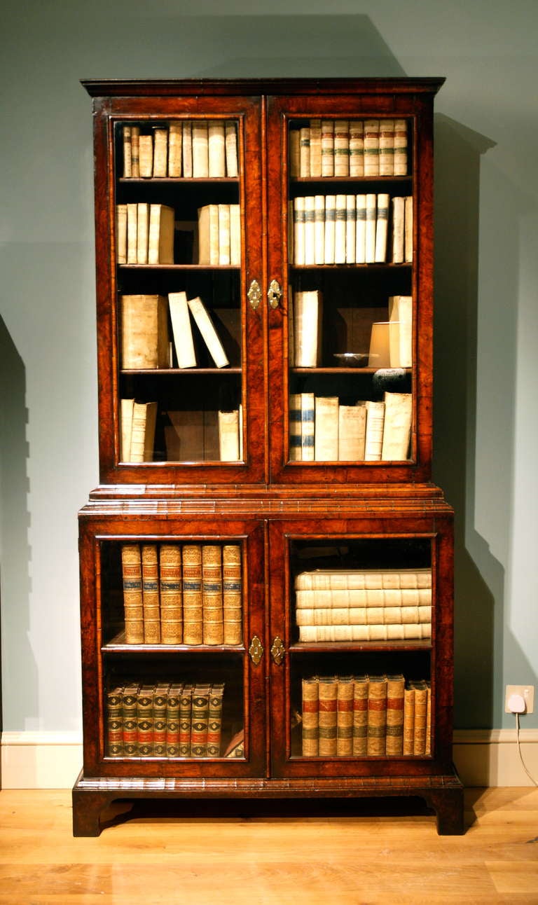 An early 18th Century English walnut display cabinet/ bookcase of rare form with finely figured walnut veneers and high quality crossgrain mouldings with bevelled glazed panels fitted to the doors of both the upper and lower sections, finely