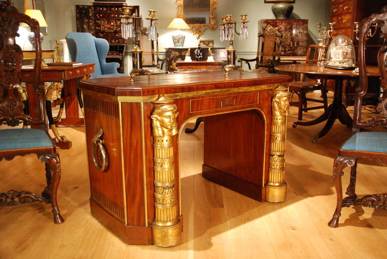 An early 19th Century leather topped mahogany parcel gilt library table in the Egyptian taste, having one dummy and one real drawer. Circa 1810.