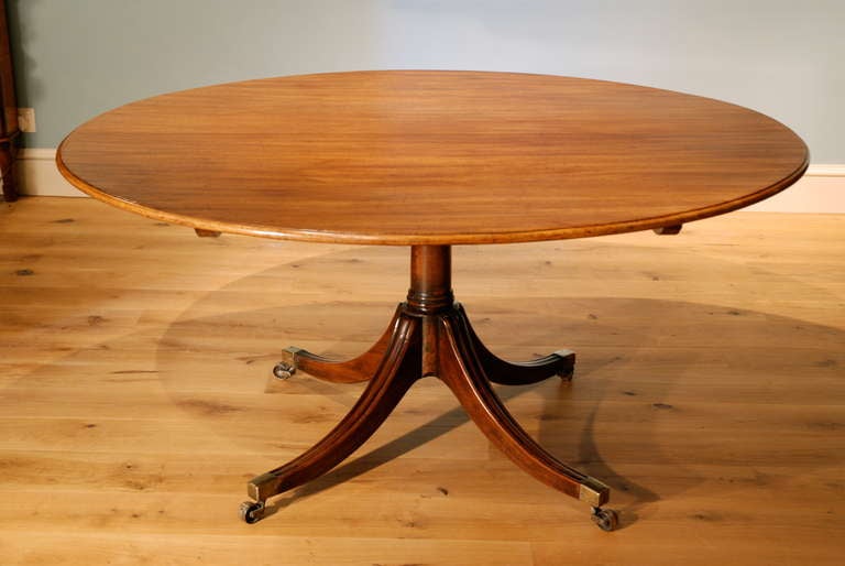 An oval mahogany tilt top breakfast table standing on gunbarrel column with four moulded outswept legs standing on brass castors to seat 6-8 people. English circa 1790.