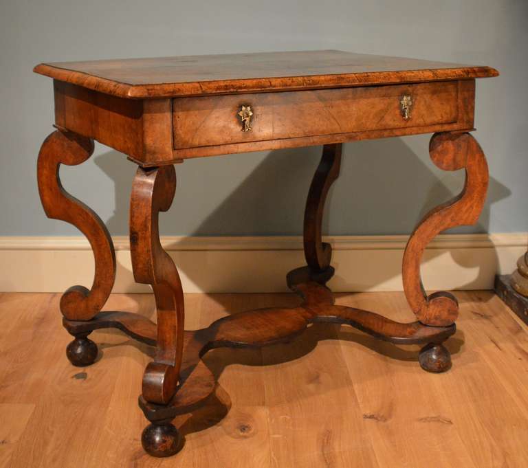 A Charles II veneered walnut one drawer side table, the top inset with an oval and with wide herringbone banding, standing on boldly scrolled legs which in turn are united by a veneered wavy X stretcher, the whole standing on it's original bun feet.