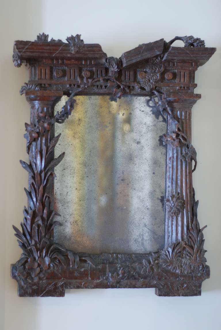 A small early 18th century carved walnut Italian 'ruined' classical mirror carved with collumns to the side rising to a 'damaged' pediment around which and from which grow naturalistically carved trailing plants. Circa 1725.