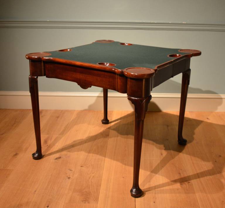A George II mahogany concertina card table, the frieze contains a drawer, the shaped top opening to reveal circular candle and oval guinea wells.