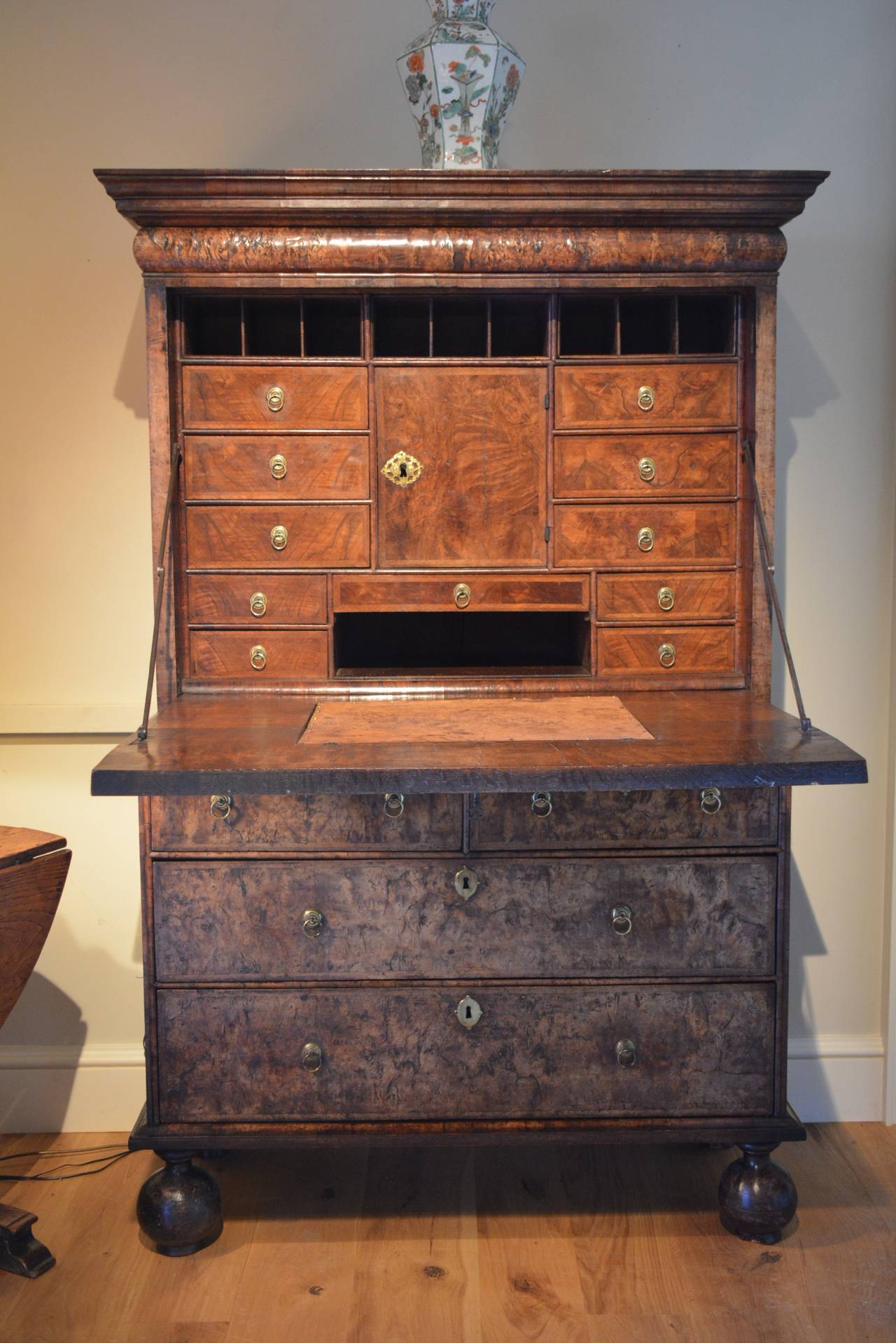 An early 18th century veneered walnut escritoire or writing cabinet of architectural form, the pulvinated frieze at the top concealing a drawer, below which the fall front opens to reveal a series of drawers and pidgeon holes around a central