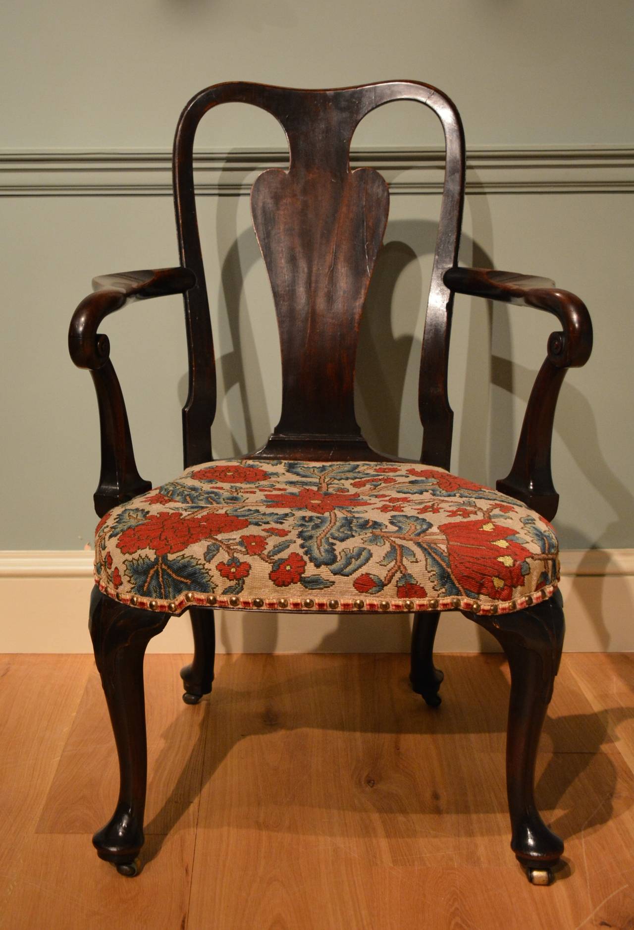 A George II mahogany armchair of exceptional drawing, the solid vase splat above the 18th Century floral needlework covered seat, cabriole legs to front and rear, with lapets carved to the front knees with pad feet and casters.
English Circa 1740