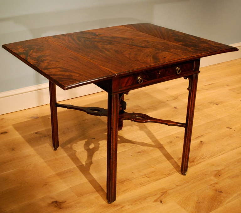 A fine mahogany Pembroke table in the Chippendale taste, the folding two flapped top veneered with mahogany of exceptional figuring, the vertically veneered frieze containing a mahogany lined drawer to one end below which are the original 'C' scroll