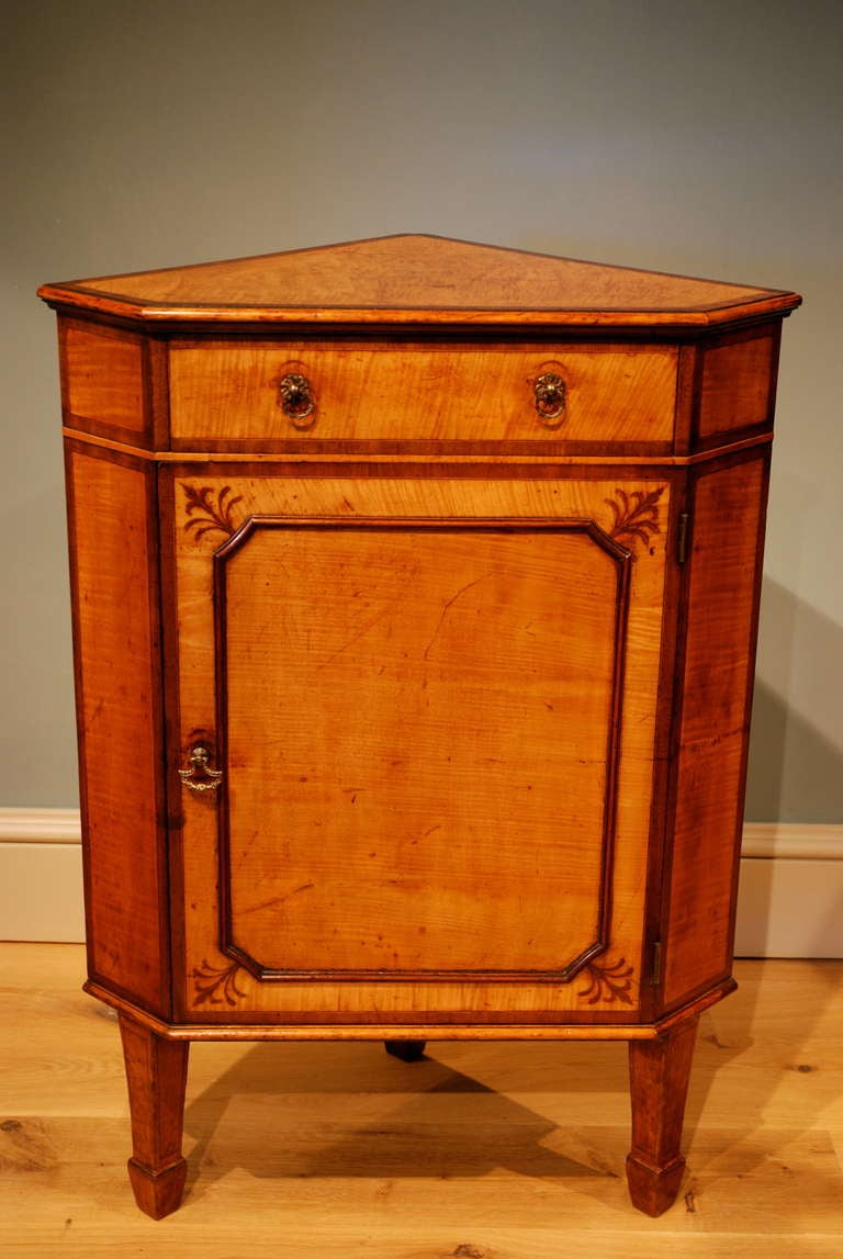 A standing corner cupboard veneered in honey coloured maple crossbanded throughout with a drawer over the cupboard below