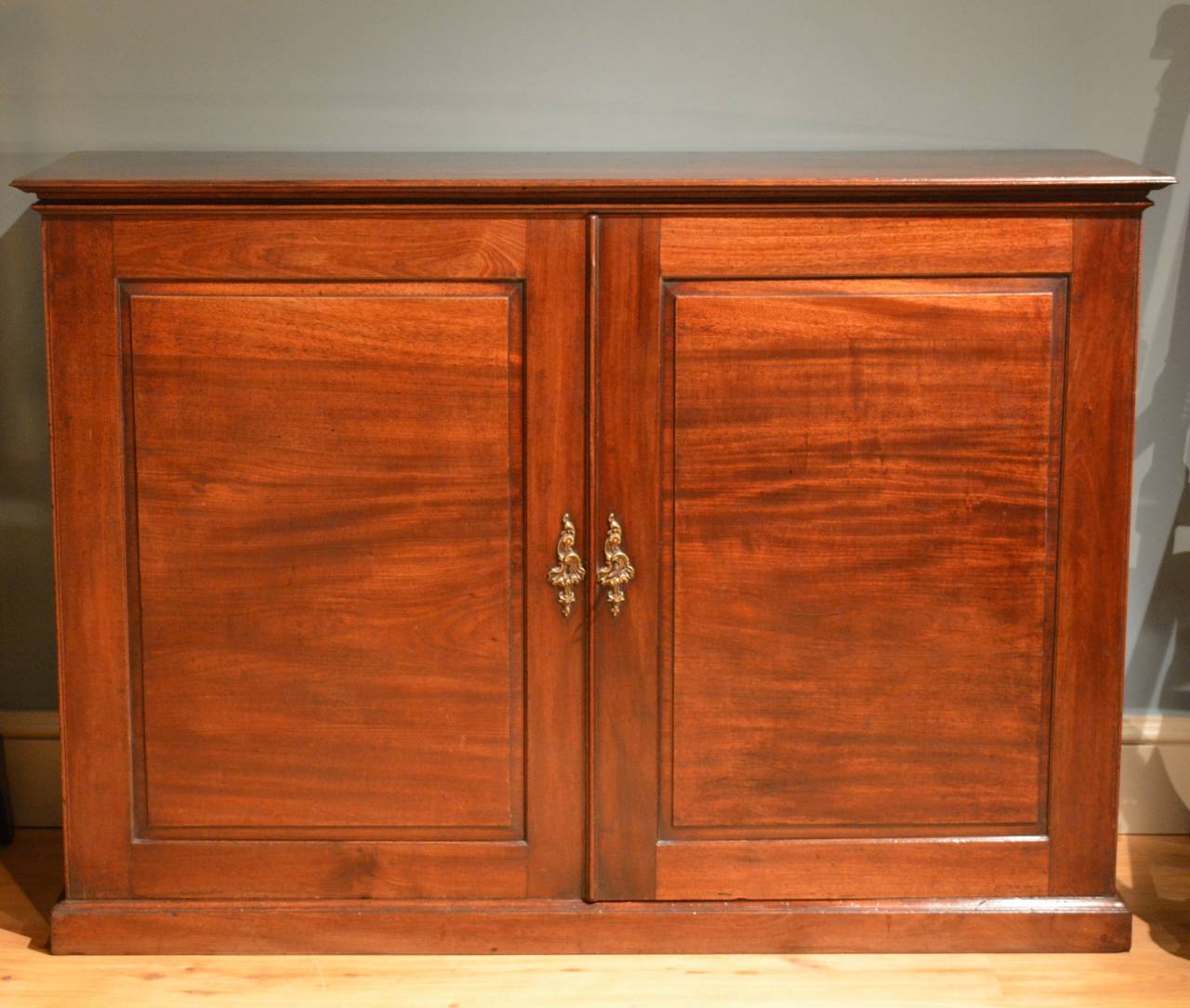 A George III mahogany two-door side cabinet, the fielded panel doors having their original Rococo escutcheons, the top and base moulds finely shaped standing on a plinth, the interior containing two adjustable shelves. This piece has particularly