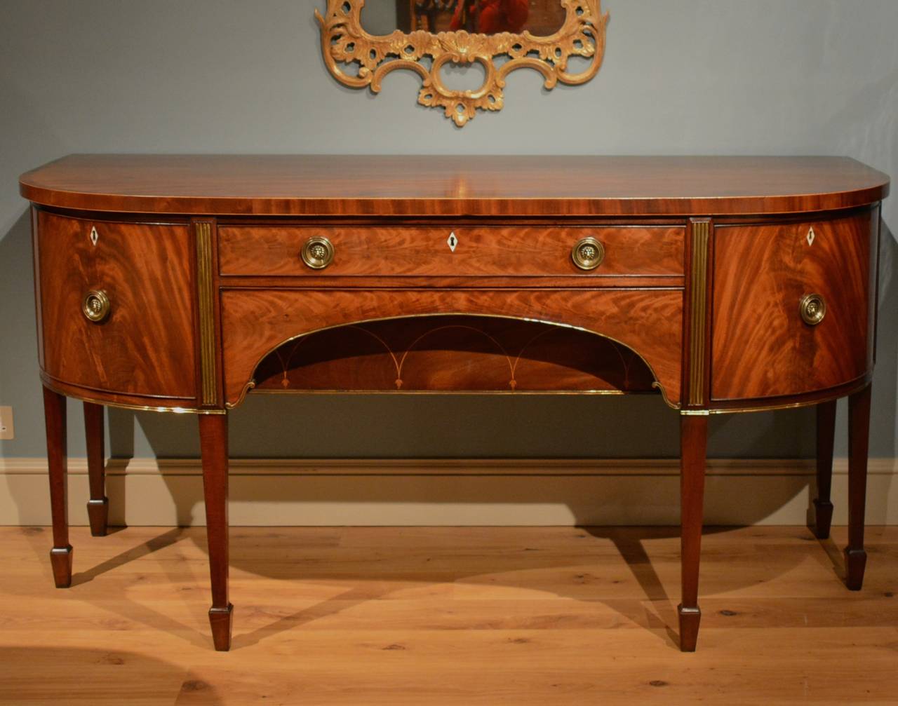 A high quality George III mahogany sideboard, the cross banded 'D-shaped' top over one deep cellarette drawer, a central long drawer and an opening cupboard, the whole finely veneered with the rare feature of added brass enrichments, standing on