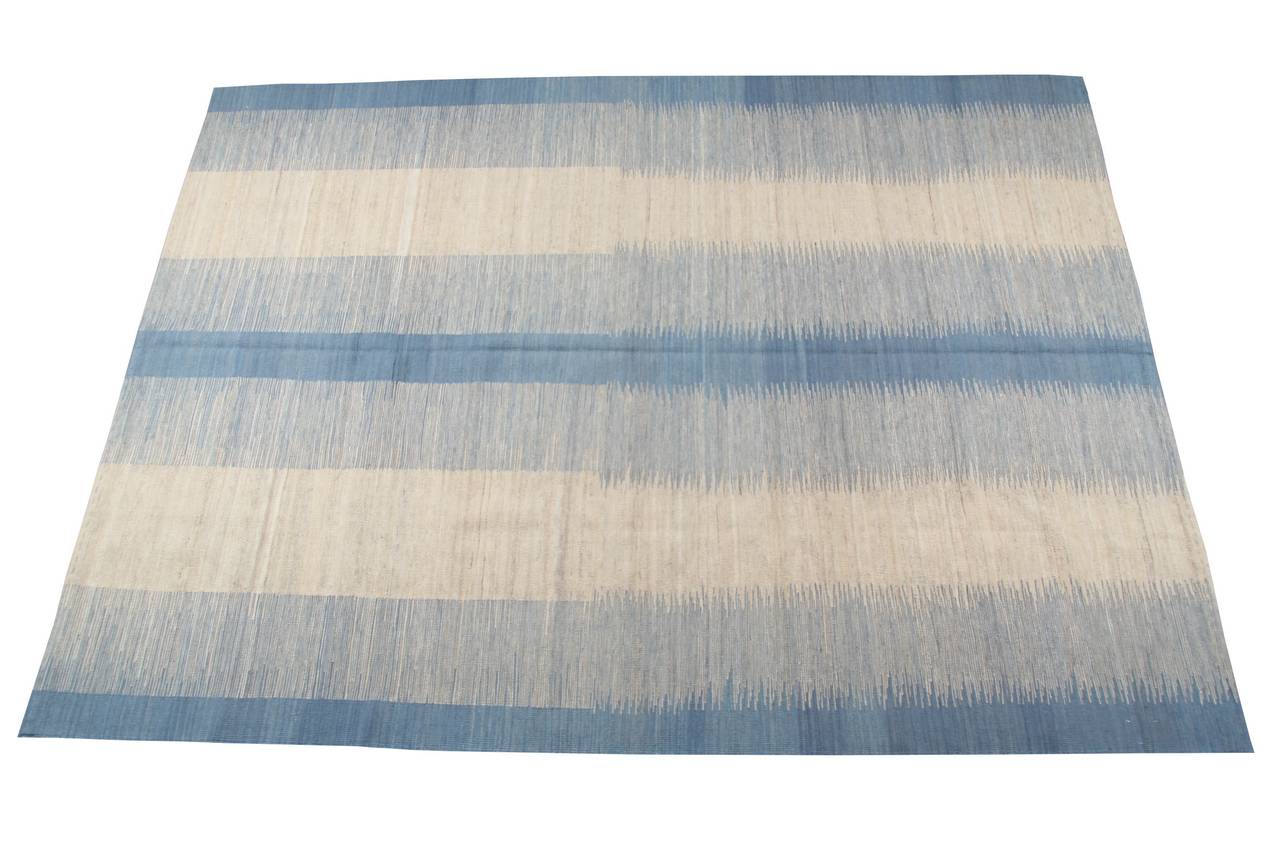 This modern Kilim follows a simple but striking design. In fact, the two main colours, light blue and white, alternate harmoniously according to asymmetric stripes.