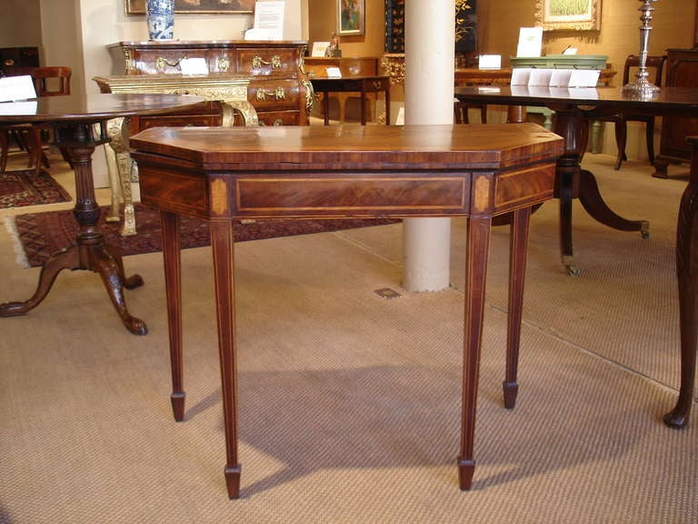 Late George III period mahogany and satinwood banded card table. The top with wide satinwood banding, the bottom portion liberally strung with boxwood, with satinwood lozenge shaped terminals at the top of the square tapering legs that terminate in