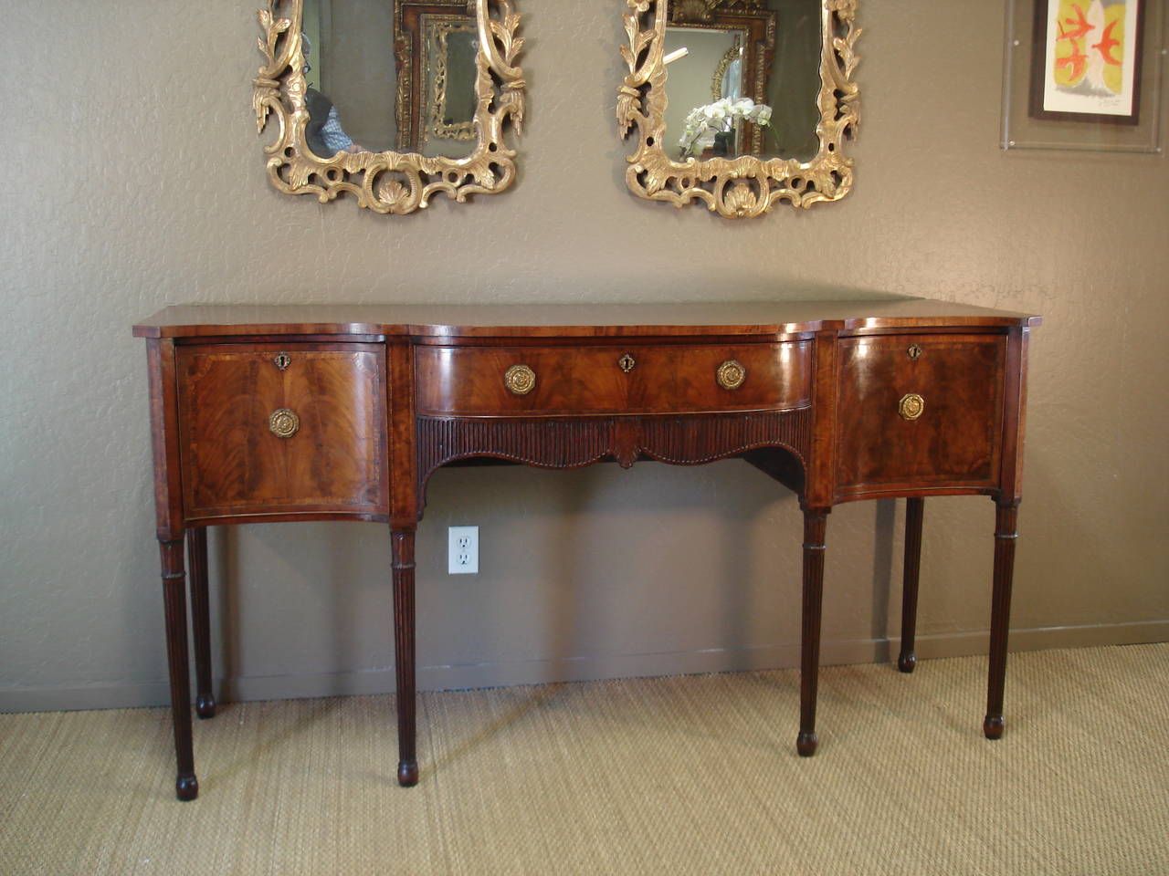 George III period mahogany sideboard of serpentine outline. The banded top above a cupboard drawer, deep drawer and shallow frieze drawer, all well figured and satinwood banded. The frieze drawer above an undulating apron of reeded decoration. The