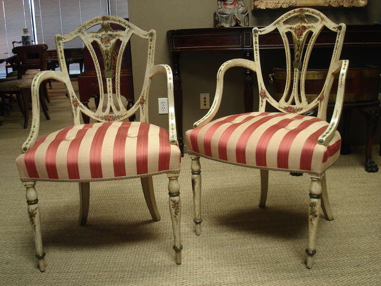 A pair of George III style painted armchairs of ample size, in the manner of Gillows. The shield back with a vase-shaped splat with painted floral decoration. The downswept arms and tapering turned legs with linked bellflowers and floral swags, all