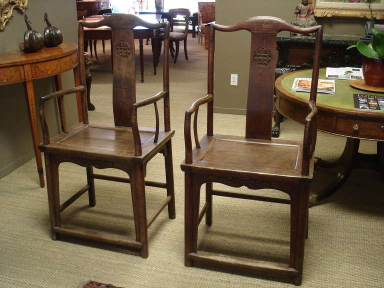 A pair of Qing period elm  yoke back armchairs. The s-form back decorated with incised medallions and with square armrests above a solid rectangular seat, raised on rounded legs joined by stretchers and a foot rest.

Qing period, probably late